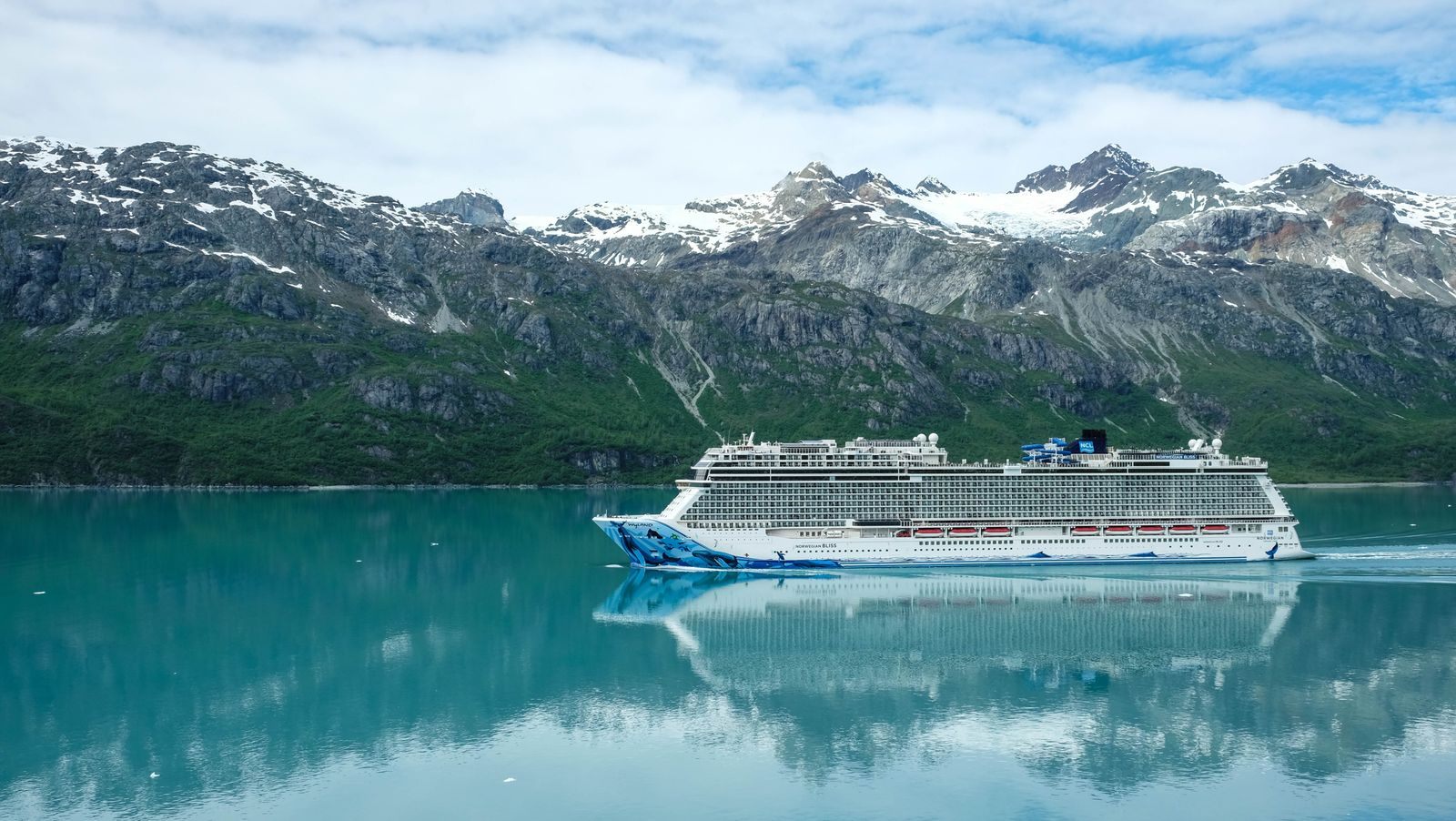 Cruise ship sailing calm water below snow-covered mountains, the view that decides the best time to cruise Alaska